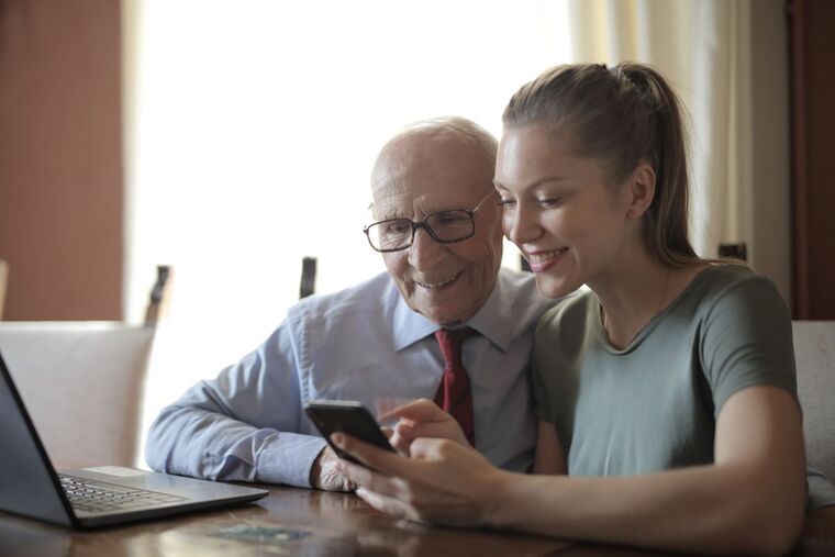 Neta sorridente mostrando o celular para o avô, que aprende com atenção