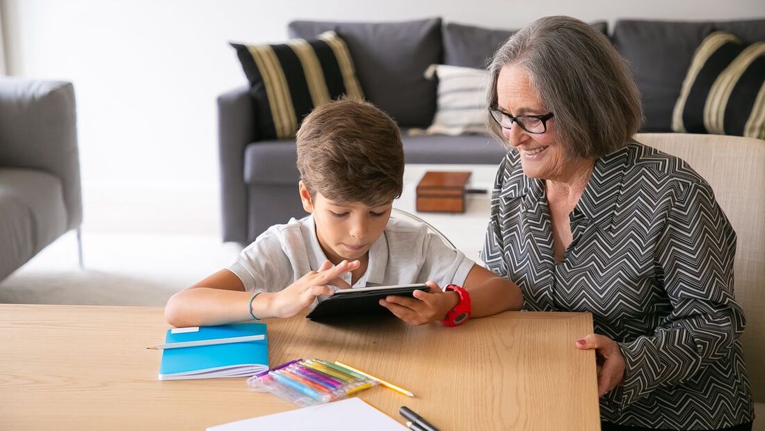 Avó sorridente acompanhando o neto que usa um tablet na sala de estar